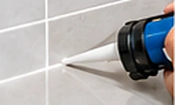Caulking gun applying a new silicone bead along tiles